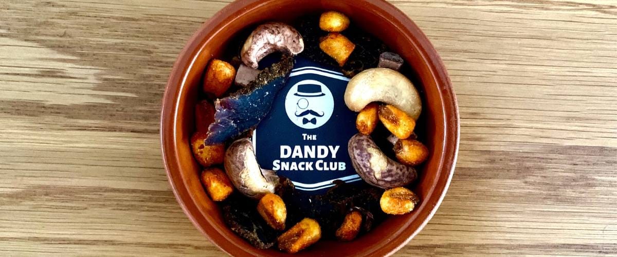 A bowl of nuts from the dandy snack club on a wooden table